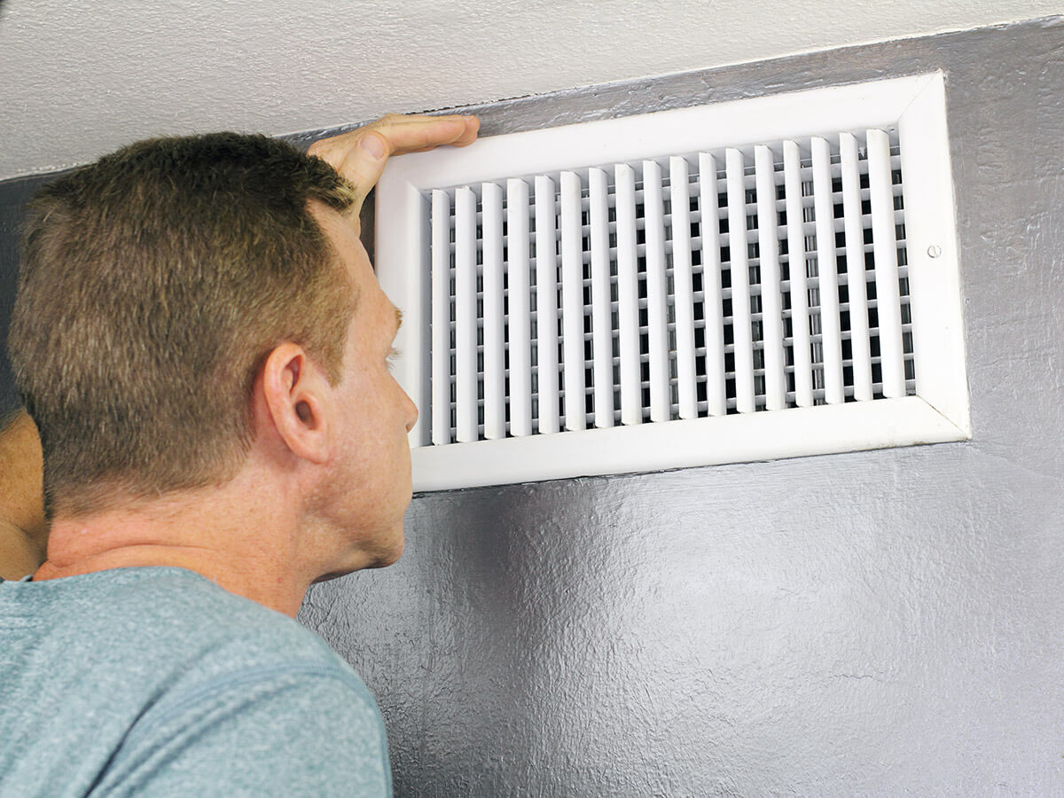 a man examining an outflow air vent grid and duct to see if it needs cleaning