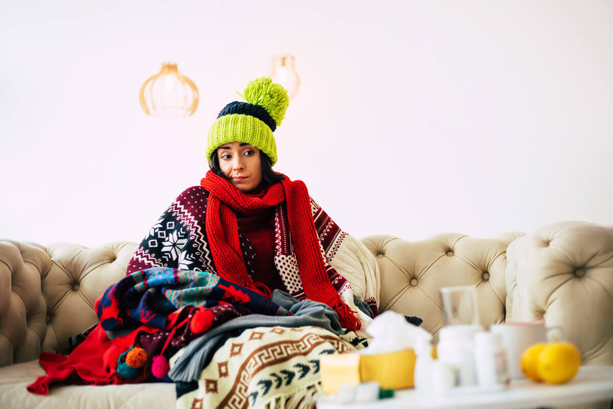 a young woman dressed in warm sweater and knitted hat sitting on a couch